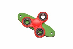 Czerwony spinner do tablicy sensorycznej na zielonej podstawce.   